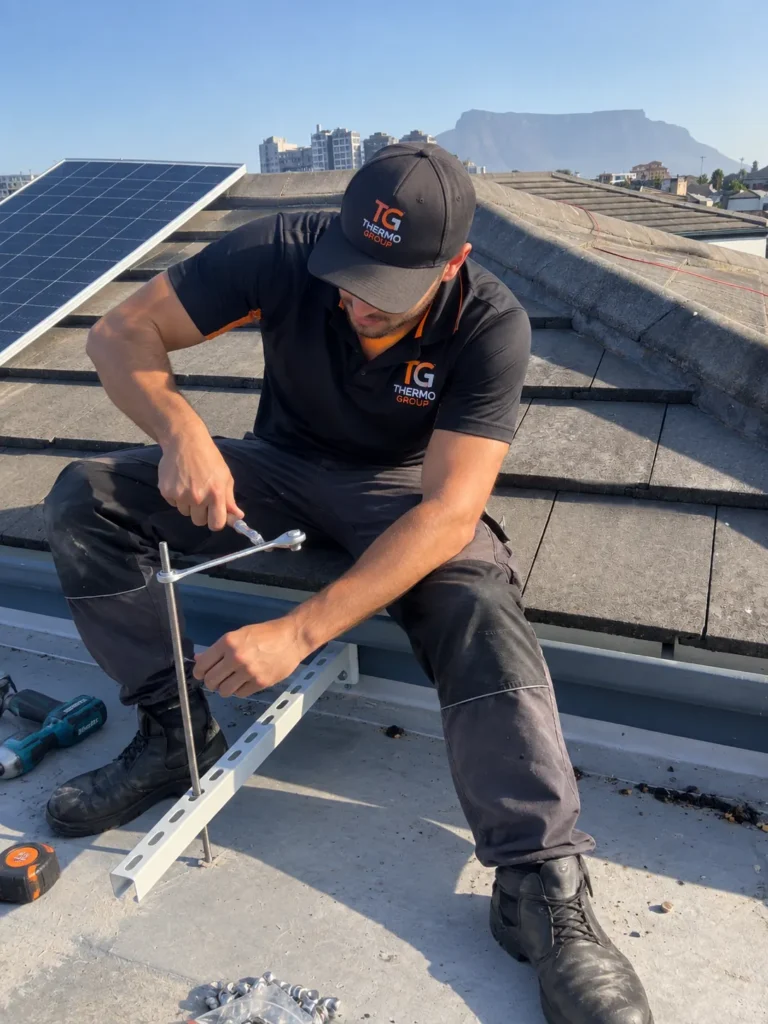 Thermo Group technician mounting solar panel rails with Table Mountain view across the bay, Table View